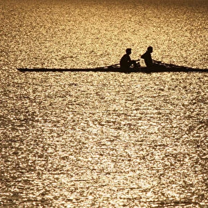 Men are silhouetted in the rising sun as they row in the waters of Sukhana Lake in
