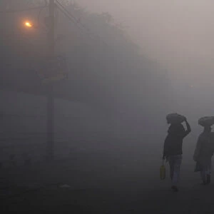 Men walk along a street on a foggy morning in the old quarters of Delhi