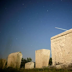 A meteor streaks past stars in the night sky above medieval tombstones during the