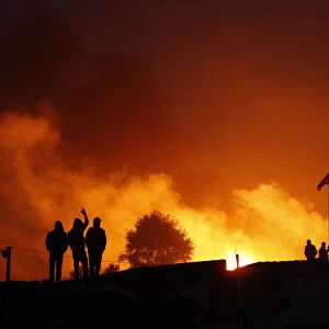 Migrants are seen in silhouette near flames from a burning makeshift shelter on the