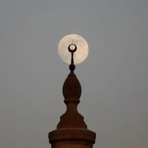 The full Moon rises over a minaret of a mosque during sunset on the 12th day of