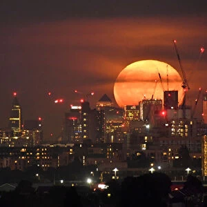 The full moon is seen rising behind skyscrapers at Canary Wharf and the London skyline