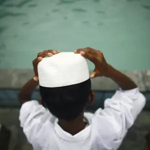 A Muslim boy puts on his hat after washing his face prior to Eid al-Fitr prayers