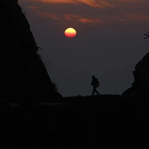 A Nepalese man is silhouetted by the setting sun as he walks along the hills at Kailali