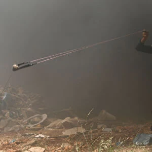 Palestinian demonstrator uses a sling to hurl stones at Israeli troops during a protest