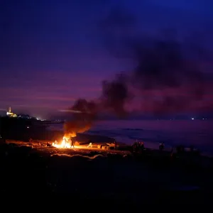 Palestinian fishermen warm themselves by a fire at a beach on a winter day