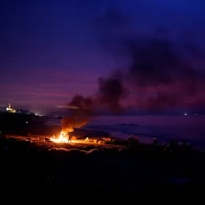 Palestinian fishermen warm themselves by a fire at a beach on a winter day