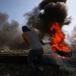 Palestinian protester moves a burning tyre during clashes with Israeli troops following a