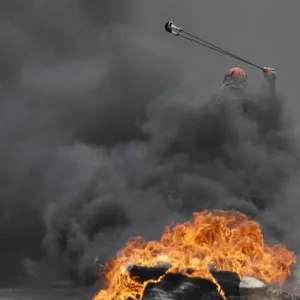A Palestinian protester uses a sling to hurl stones towards Israeli troops during clashes