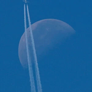 A passenger plane flies in the sky as the Moon is seen in Berlin