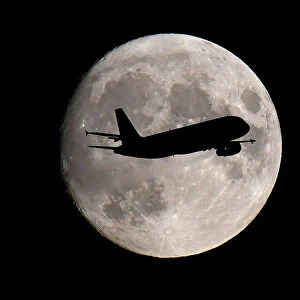 A passenger plane passes in front of the moon as it makes its final landing approach