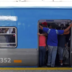 Passengers stand on the edge of a commuter train door at the Once train station in Passengers stand on the edge of a commuter train door at the Once train station in