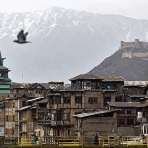 People cross a footbridge in front of cluster of traditional houses in Srinagar