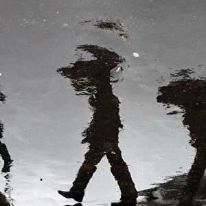 People holding umbrellas are reflected in puddles of rain at the Vatican Radio