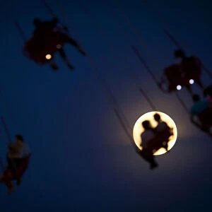 People ride the Luna Park Swing Ride as the Super Moon rises on Coney Island