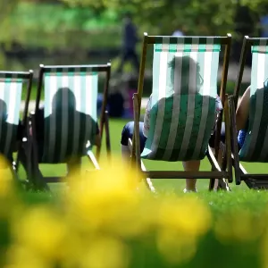 People are silhouetted against the fabric of deckchairs as they enjoy the sunshine in St
