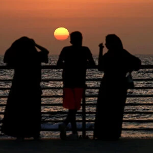 People stand on the corniche at sunset in Jeddah