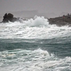 People standing on the Pointe de la Torch peninsula watch waves breaking on the Brittany People standing on the Pointe de la Torch peninsula watch waves breaking on the Brittany