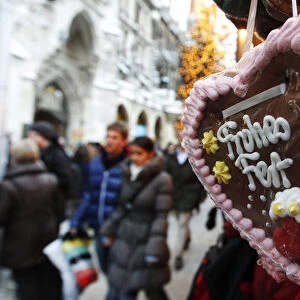 People walk past a gingerbread pastry reading happy celebration at a market in Munich