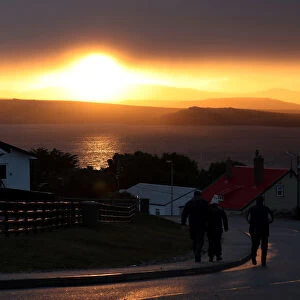 People walk down a road at sunset in Port Stanley