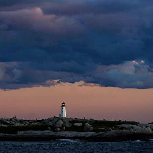People walk on the rocks at the lighthouse at dusk in Peggys Cove