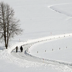 People take a walk along snow covered fields during sunny winter weather in Oberstdorf