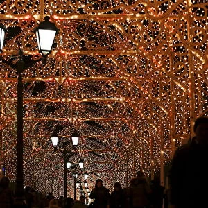 People walk along a street decorated with festive illumination lights, part of the New Year