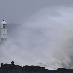 People watch as large waves crash against the seawall during strong winds at Porthcawl
