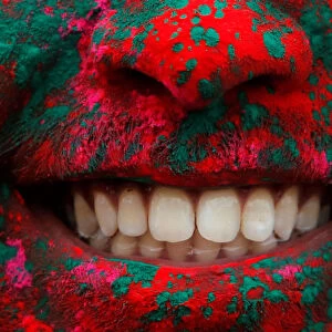 A person smiles after being covered in colored powder during a Holi festival party
