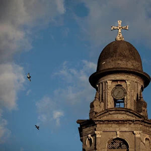 Pigeons fly past a stopped clock tower marking the time of the 1972 earthquake in the old