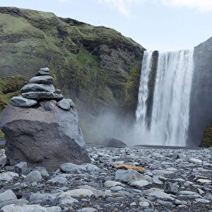 A pile of rocks stand in front of a waterfall in Skogarfoss, Iceland