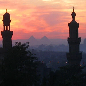 Pyramids of Giza appear between two minarets during a warm winter sunset in Cairo
