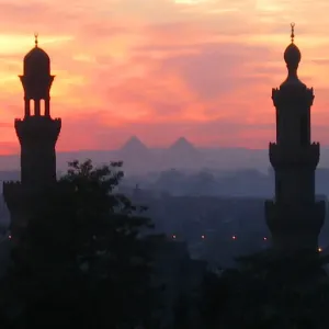 Pyramids of Giza appear between two minarets during a warm winter sunset in Cairo