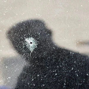 The reflection of a man is seen on a shattered car windscreen after a bomb blast in the
