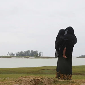 A Rohingya refugee woman protects her son from rain as she looks towards the beach after
