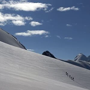Roped parties of climbers walk on a glacier marking the border between Switzerland