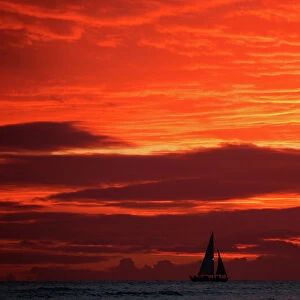 A sailboat passes in front of clouds lit up by the sunset sky off Waikiki in Hawaii, U. S