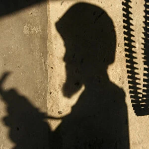 The shadow of an Afghan National Army soldier and bullets are cast on the wall of