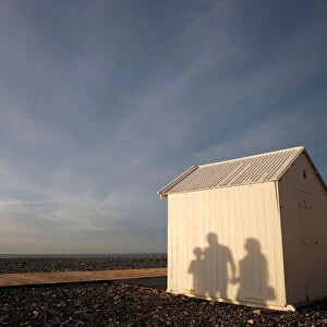A shadow of a family is seen on a beach cabin on the pebbled beach during sunset in
