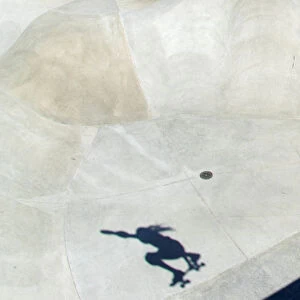 The shadow of a skateboarder is cast at the bottom of a cement bowl