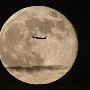 A silhouetted airplane flies past a super moon over New York