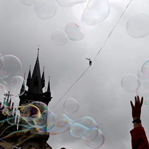 Soap bubbles float as a man balances on a line stretched over the Old Town Square in