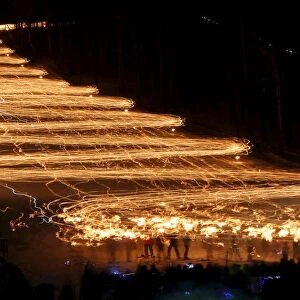 Spectators watch hundreds of skiers descend from a slope while holding lit torches in the