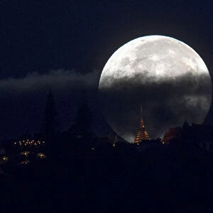The supermoon is partly covered by clouds as it sets behind Wat Phrathat Doi Suthep in