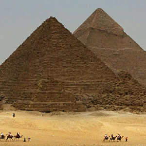 Tourists ride camels in front of Giza pyramids