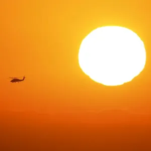 A U. S. military helicopter travels over the pacific ocean past a setting sun near Cardiff A U. S. military helicopter travels over the pacific ocean past a setting sun near Cardiff