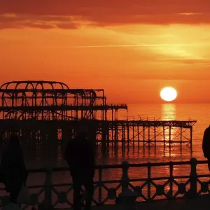 Visitors watch the sun set behind the remains of the West Pier on the seafront at Brighton Visitors watch the sun set behind the remains of the West Pier on the seafront at Brighton