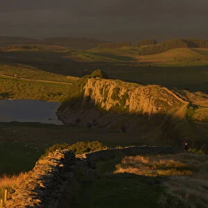 A walker looks north towards Scotland in late evening sun at Hadrians Wall near Crag