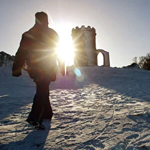 A WALKER STRIDES THROUGH SNOW TOWARDS THE OLD JOHN MEMORIAL IN BRADGATE PARK