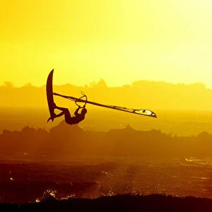 WINDSURFERS GETS AIRBOURNE AS THE SUN SETS ON CAPE TOWNs BLaUBERG BEACH